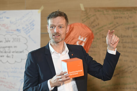 A person speaks. She is holding an orange cube in her hand.