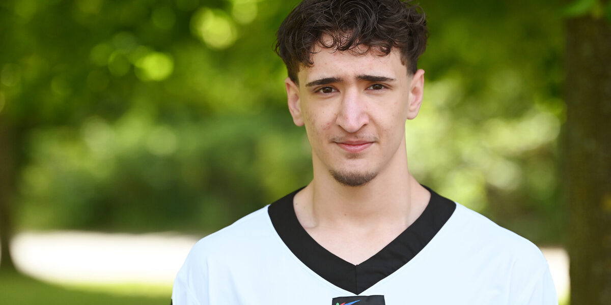 A man in a white top with a black collar and the German flag on his sleeve looks into the camera.