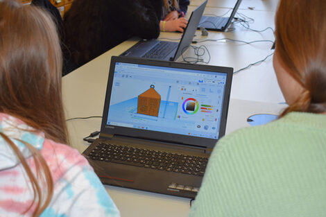 Two girls look at a laptop showing the simple design of a house.