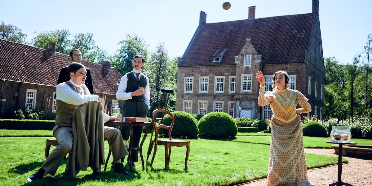 Eine Frau wirft einen Ball vor einem historischen Gebäude. Drei Männer beobachten sie kritisch.