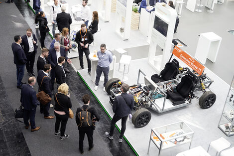 A bird's eye view shows several people standing in front of a vehicle at an exhibition stand.