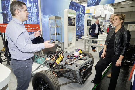 Two people are standing at an exhibition stand with a vehicle.