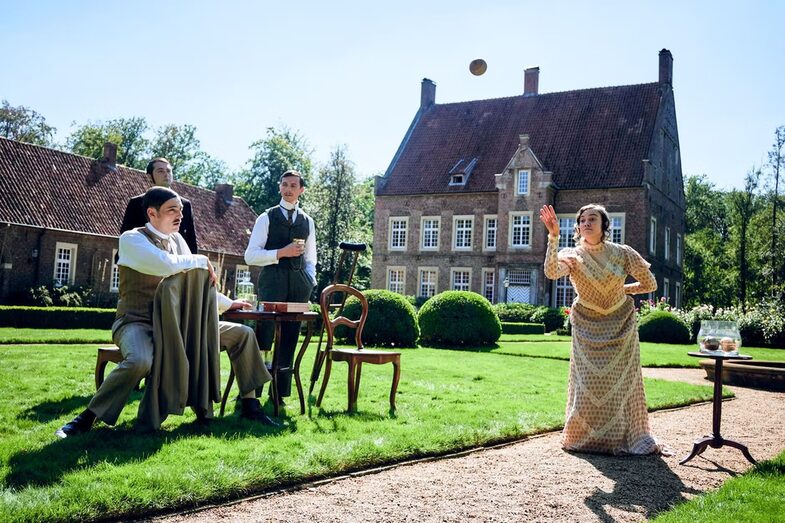 A woman throws a ball in front of a historic building. Three men watch her critically.