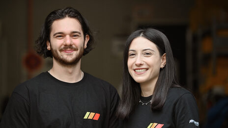 Zwei Personen in schwarzen T-Shirts im Porträt vor einem dunklen Raum im Hintergrund.