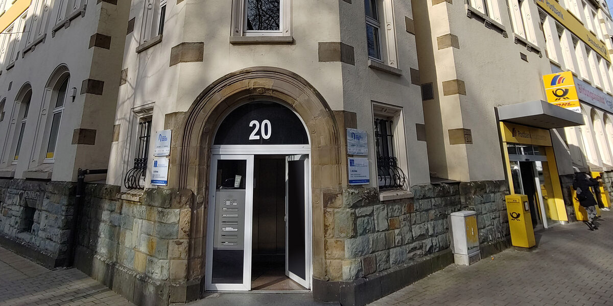 A door is open in a corner house with the number 20, next to it you can see a branch of the post office.