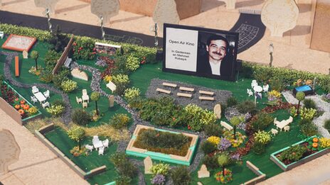 Ein Miniaturmodell eines öffentlichen Platzes zeigt eine parkähnliche Anlage mit Beeten und Sitzbänken. In der Mitte erhebt sich eine Leinwand, auf der das Porträt eines Mannes zu sehen ist.
