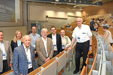 Eine Gruppe Menschen steht in einem Hörsaal. Auf der Leinwand ist der Schriftzug "IEEE IDAACS 2023" zu lesen.