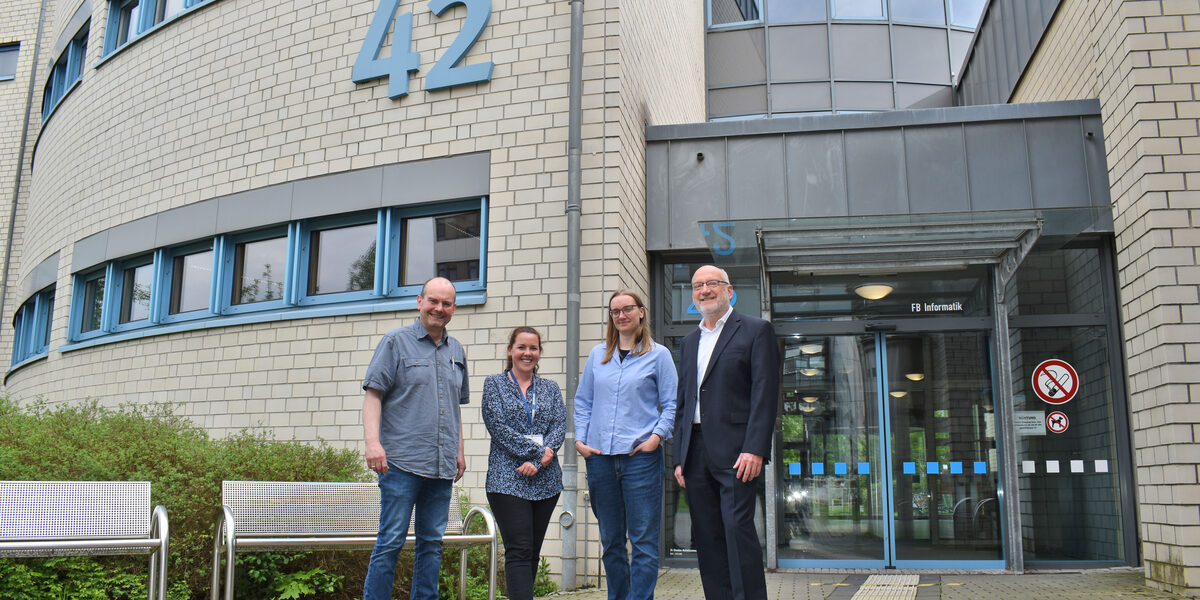 Four people are standing in front of the IT building at number 42.