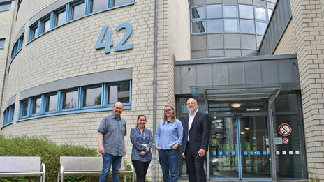 Four people are standing in front of the IT building at number 42.