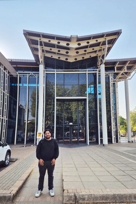 Eine Person steht vor einer markanten Fassade aus Glas und Stahl.