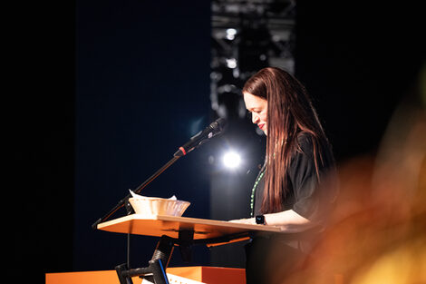 A person stands at a lectern and looks at their notes with a smile.