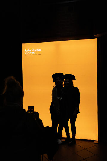 Zwei Personen im Gegenlicht vor einer orange leuchtenden Wand.