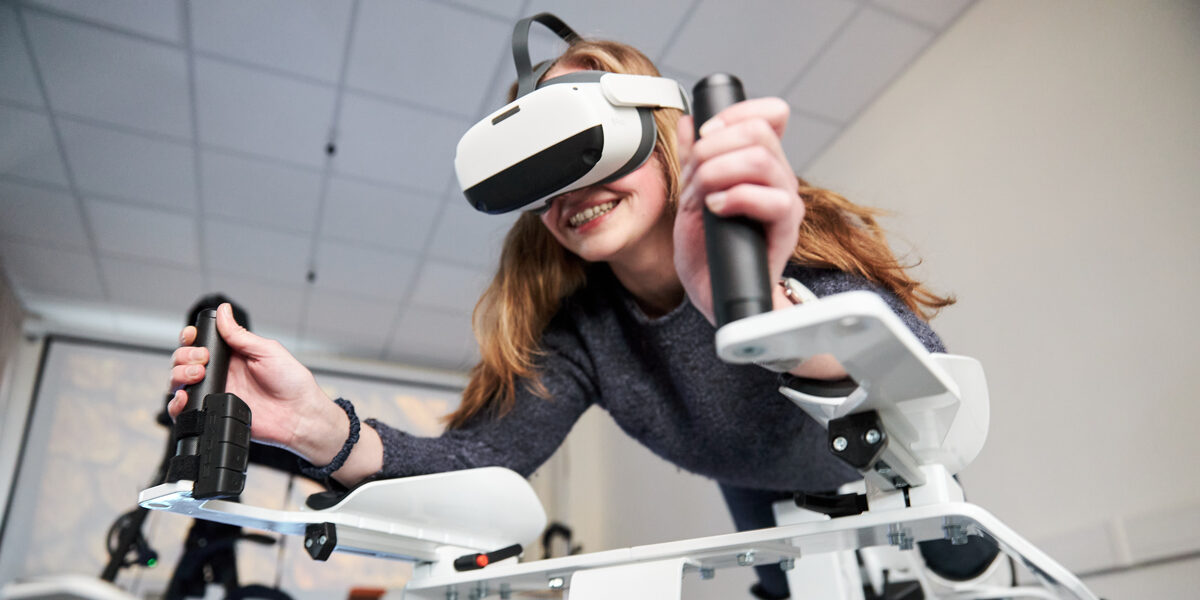Photo of a person on the Icaros device. She is wearing VR goggles and holding on to the handles.
