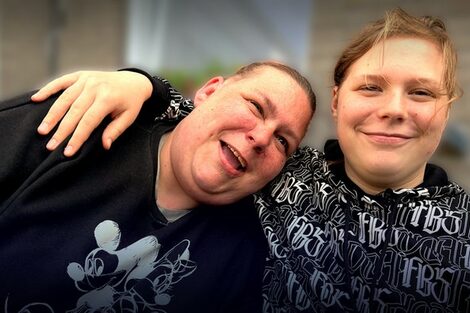 Mutter und Tochter lachen. Die Tochter legt den Arm um die Mutter.
