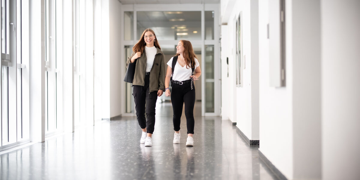 Photo of two girls running down the hallway laughing. __ Two girls run down the hallway laughing.