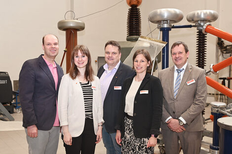 Five people in front of technical devices in a high interior.