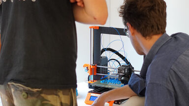 Zwei Personen blicken auf einen 3D-Drucker.