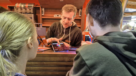 One person shows a tablet to two people in front of them.