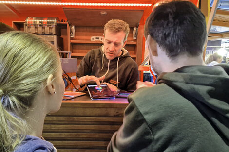 Eine Person zeigt zwei Personen vor sich ein Tablet.
