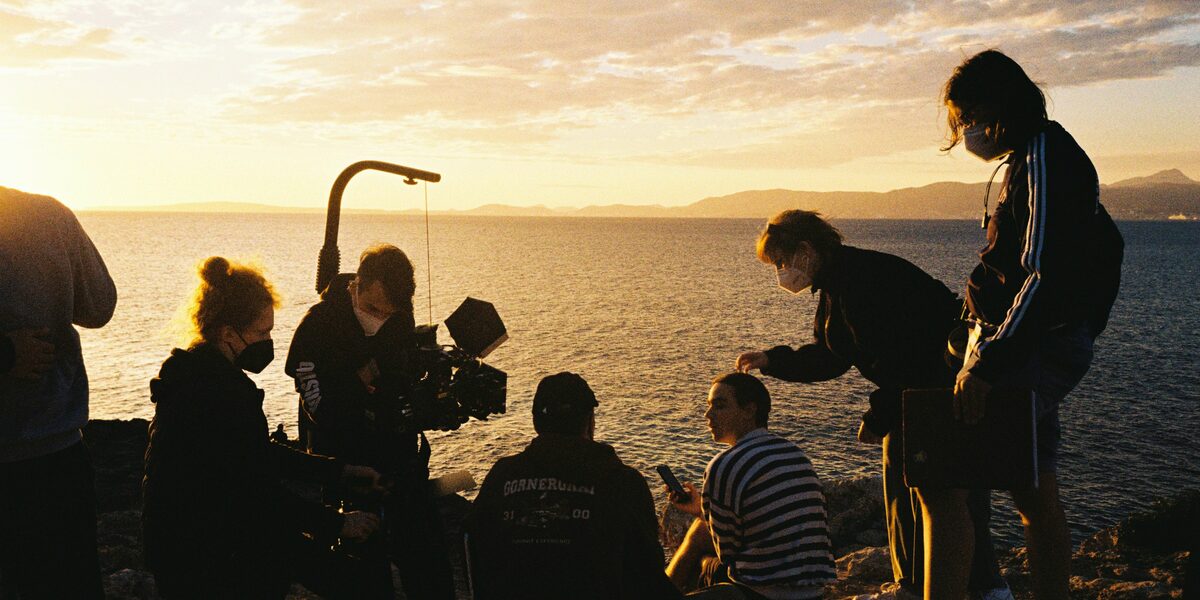 Eine Filmcrew steht am Strand vor einem Sonnenuntergang.