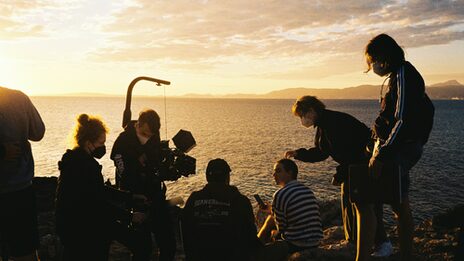 Eine Filmcrew steht am Strand vor einem Sonnenuntergang.