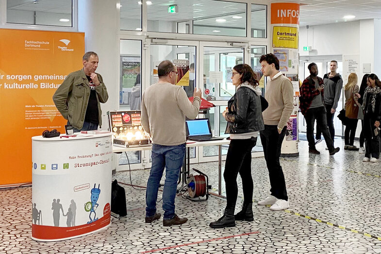 Several people are standing at an information stand in the foyer at Sonnenstrasse 100.