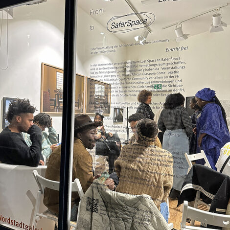 View through a shop window into a room where people are talking to each other. "Safer Space" is written on the window pane.