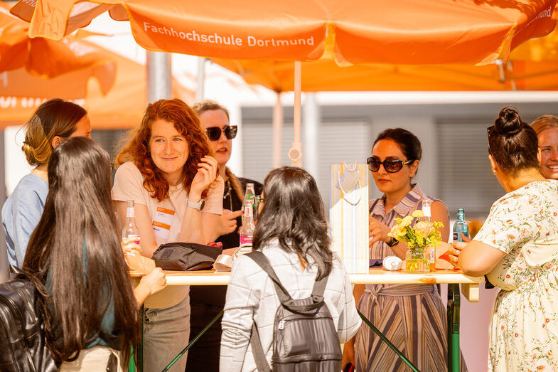 Promovierende unterhalten sich bei sommerlichem Wetter unter einem Sonnenschirm