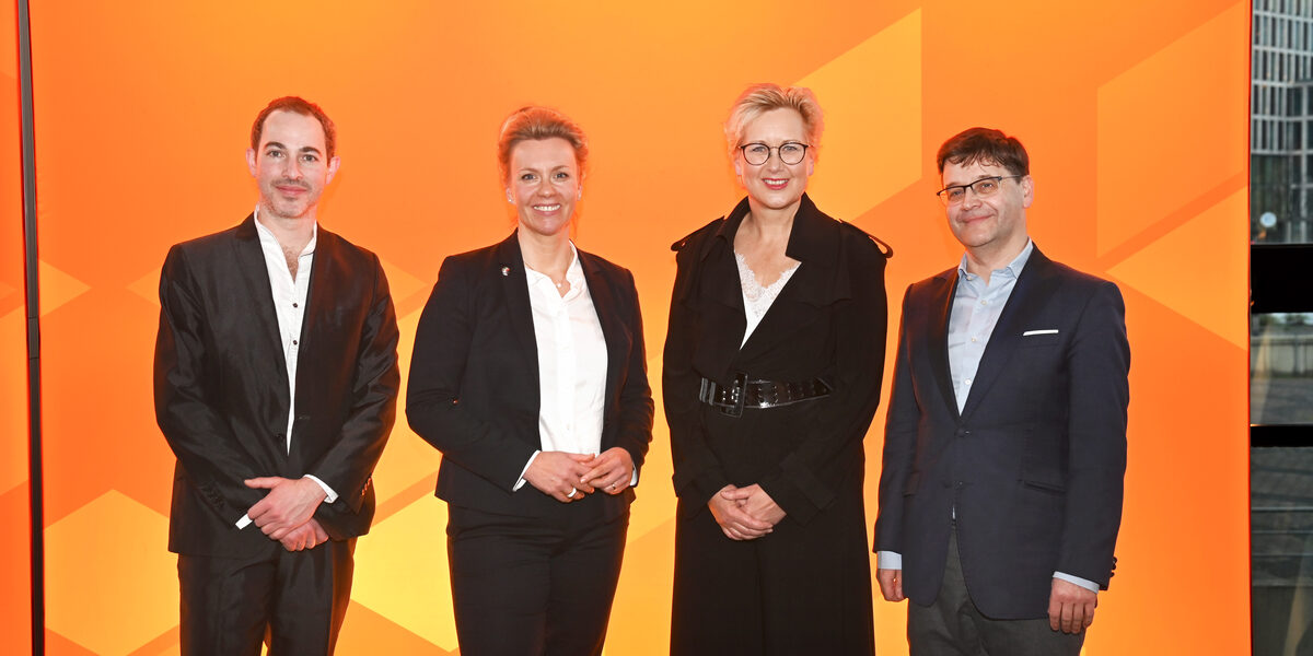 Four people stand next to each other in front of an orange UAS wall.