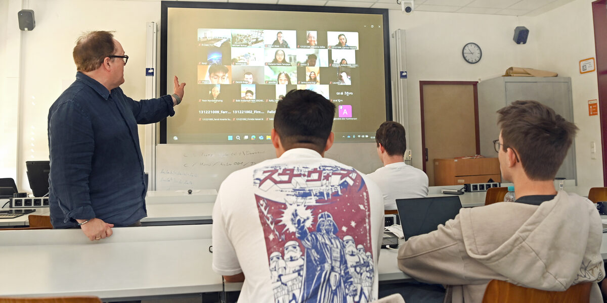 People sit in a seminar room and look at a screen on which other people are connected.