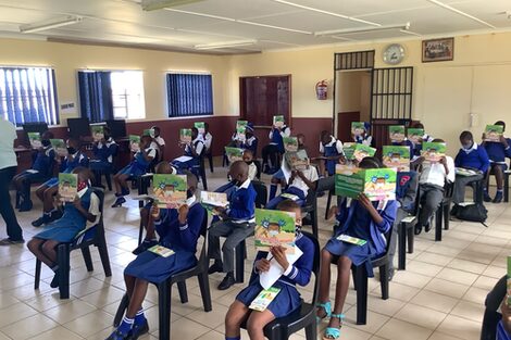 Children sit neatly on chairs in their classroom at school and hold up the coloring book.