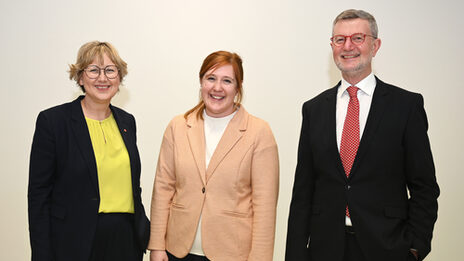 Three people against a white background look smiling into the camera.