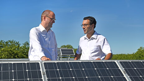 Two people are standing on the roof of Fachhochschule Dortmund at the solar system and talking.