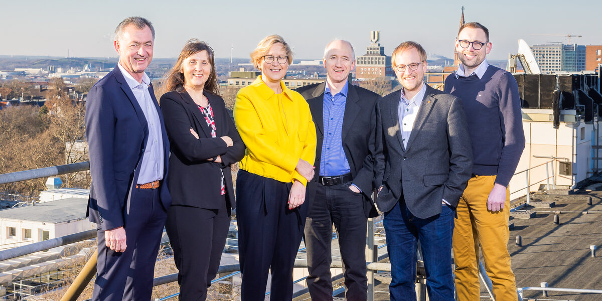 A group of people stand on the flat roof of Fachhochschule Dortmund's Sonnenstraße campus. The city can be seen in the background.