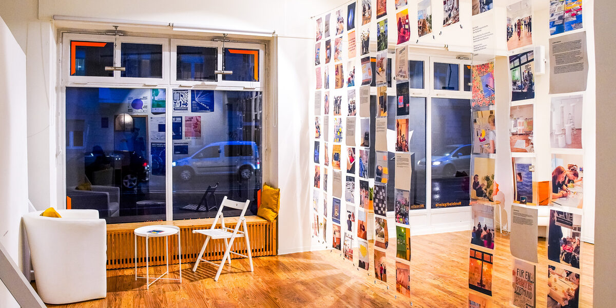 A wall of transparent transparencies, on which photos of past events have been printed, hangs in the middle of the room.