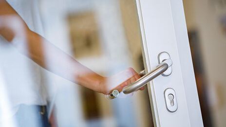 Foto einer weiblichen Hand, die die Klinke einer Tür mit Glasscheibe herunterdrückt.__ Female hand opens a door.