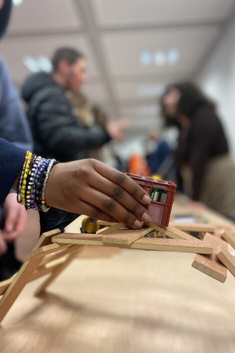 A pupil places a miniature drinks crate on a small Leonardo bridge made of wooden sticks.