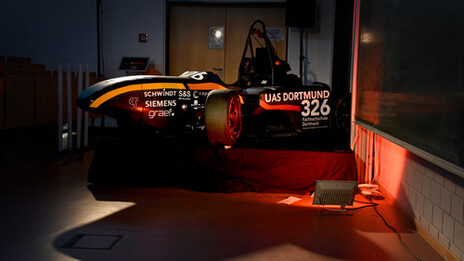 The nose of a racing car, half covered by a red cloth, against a black background.