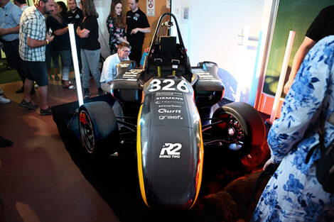 A racing car on a platform surrounded by people.