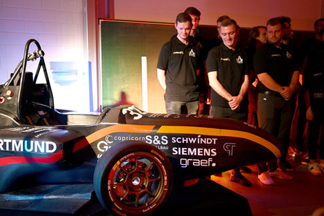 Several people in black T-shirts look at a racing car.