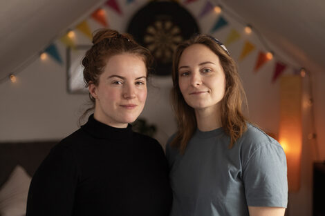 Two people stand next to each other in front of a decorated wall.