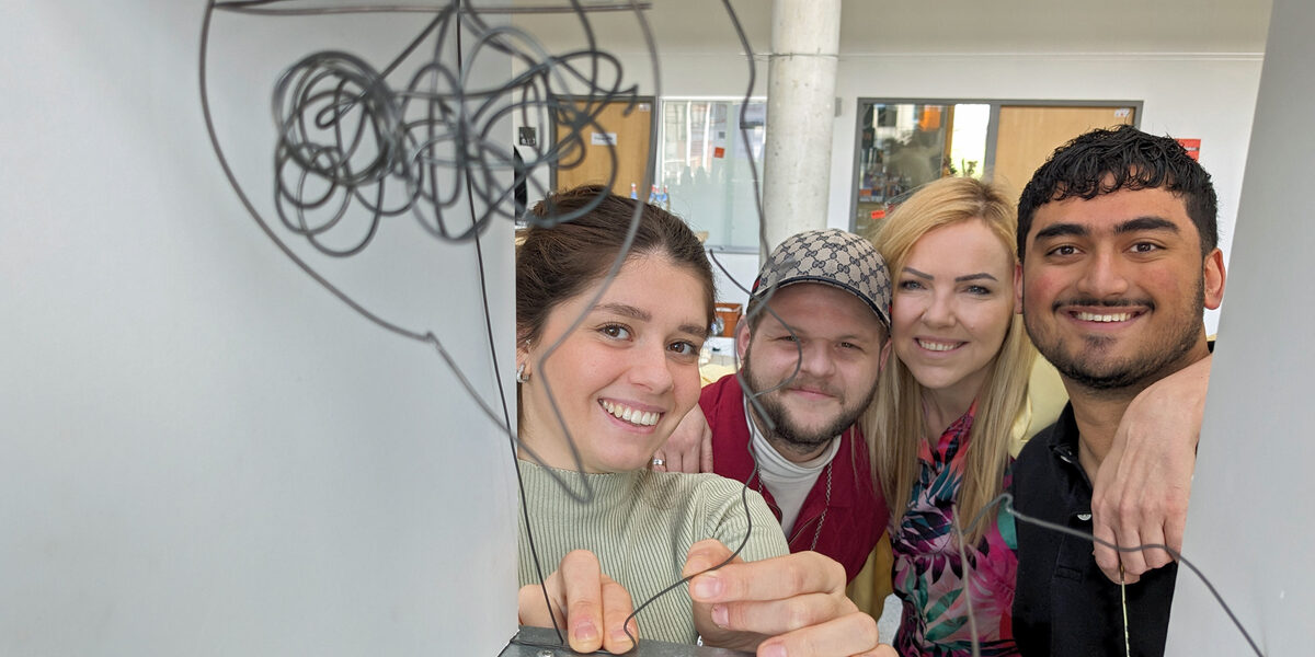 Four people look through a metal box in which they have hung their wire construction.