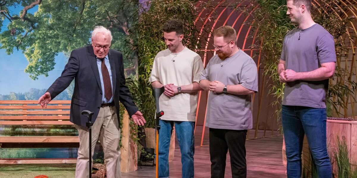 An older man shows how his walking stick remains standing on its own. Three young men look on.