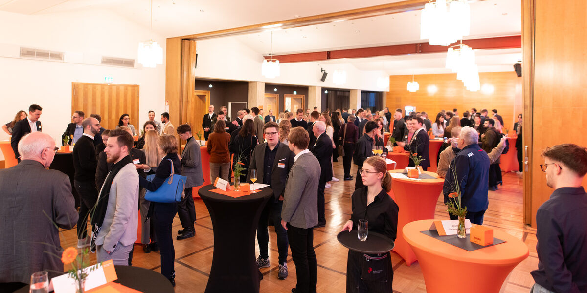 In a large room, several people are standing at tables and chatting.