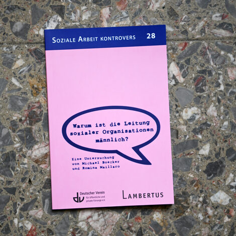 Ein Buch mit dem Titel "Warum ist die Leitung sozialer Organisationen männlich?" liegt auf einem Steinfußboden.