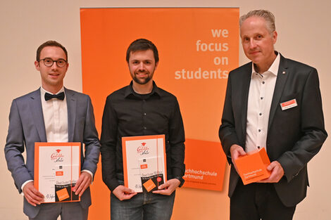Drei Personen stehen vor einem Aufsteller mit der Aufschrift "we focus on students".