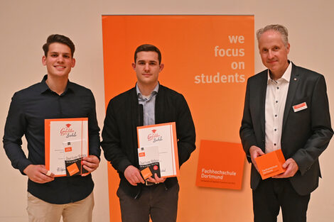Drei Personen stehen vor einem Aufsteller mit der Aufschrift "we focus on students".