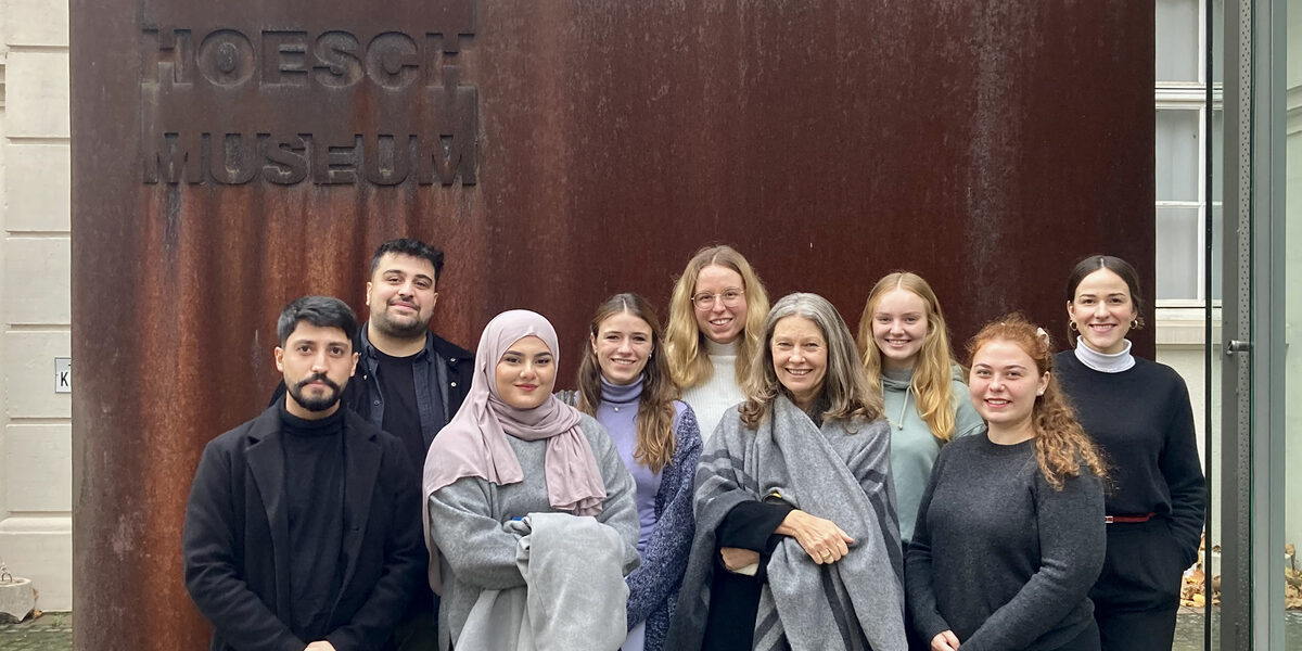 Group of students with Professor Diana Reichle in front of the entrance sign to the Hoesch Museum.
