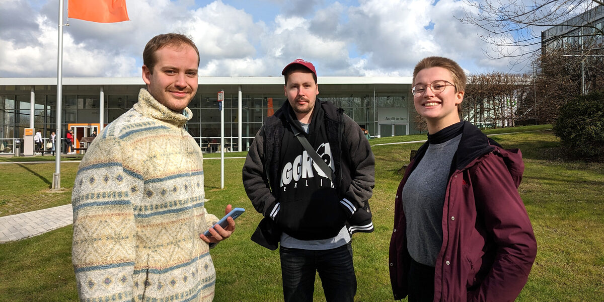 Three people are standing on a meadow on the UAS campus on Emil-Figge-Straße and talking to each other.