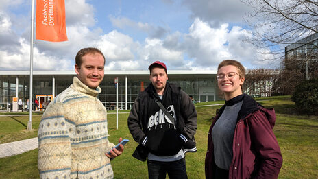 Three people are standing on a meadow on the UAS campus on Emil-Figge-Straße and talking to each other.